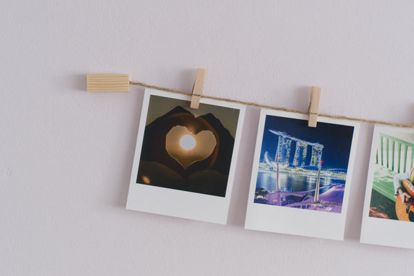 A wall mounted photo display line with natural wood and twine, hanging three instant photos with clothes pegs.