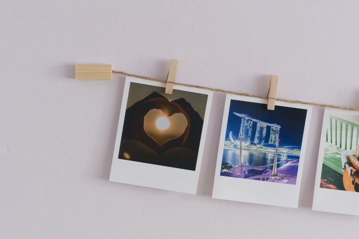A wall mounted photo display line with natural wood and twine, hanging three instant photos with clothes pegs.