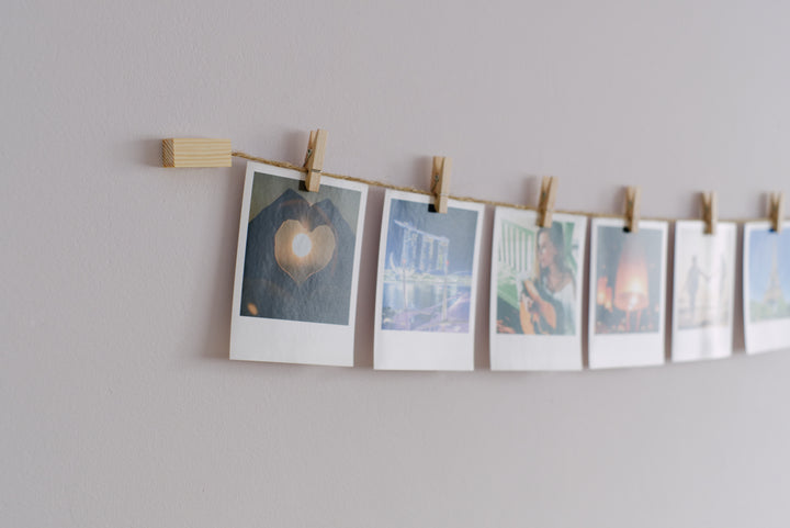 A natural wood and twine wall mounted photo display with instant photos hung up with clothespins