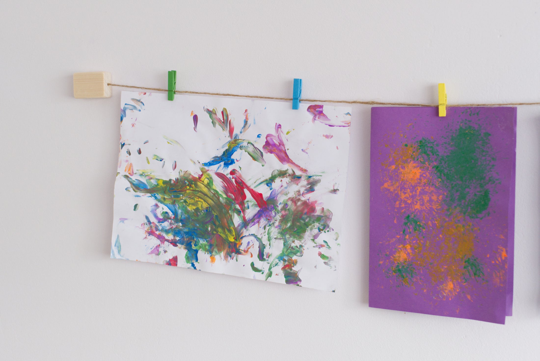 Kids art display with colourful mini clothespins hanging up two pieces of artwork