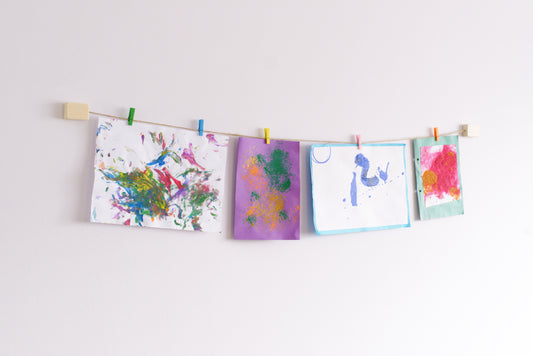 children's artwork hanger made of wood and twine hanging up pictures with colourful wooden clothes pegs