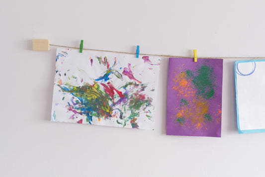 A wall-mounted art display featuring kids  art work with colorful mini clothes pegs and natural jute twine hanging line.